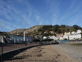A sandy beach with a promenade and multi-story buildings at the base of a rocky hill at Gerrard House Apartment in Llandudno