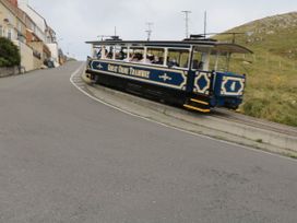 A tram with passengers on a track next to a road and residential buildings at Gerrard House Apartment in Llandudno