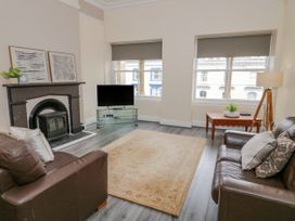 A living room with two brown sofas a fireplace a TV on a glass stand a wooden table and two windows with gray blinds at Gerrard House Apartment in Llandudno