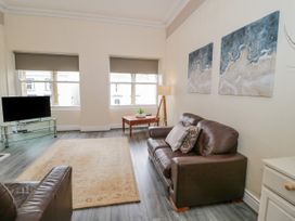 A living room with two brown leather sofas a rug a wooden side table with a lamp and a TV on a glass stand at Gerrard House Apartment in Llandudno