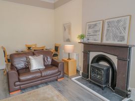 A living room with a brown leather sofa two pillows a wooden dining table with four chairs a fireplace with decorative items and a lamp on a wooden side table at Gerrard House Apartment in Llandudno