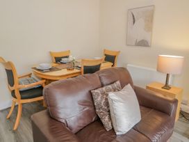 A brown leather sofa with cushions next to a wooden dining table with chairs a lamp and wall art at Gerrard House Apartment in Llandudno