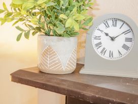 A plant in a decorated pot next to a clock with roman numerals on a wooden surface at Gerrard House Apartment in Llandudno