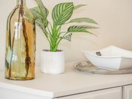 A white cabinet with a decorative bottle a potted plant and a white dish on a silver tray at Gerrard House Apartment in Llandudno