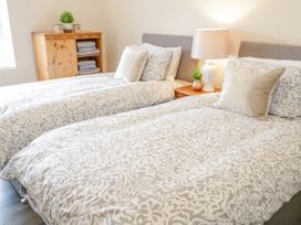A bedroom with two beds side by side a nightstand with a lamp and a wooden cabinet with towels at Gerrard House Apartment in Llandudno