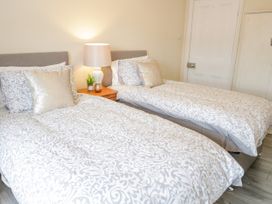 A bedroom with two beds a nightstand lamp and door at Gerrard House Apartment in Llandudno
