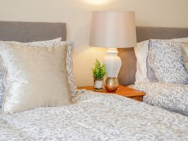 Two beds with patterned bedding and pillows with a bedside table with a lamp plant and decorative item at Gerrard House Apartment in Llandudno
