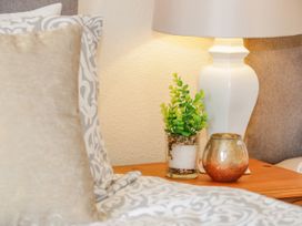 A bedside table with a white lamp green plant and decorative candle next to a bed with patterned bedding at Gerrard House Apartment in Llandudno