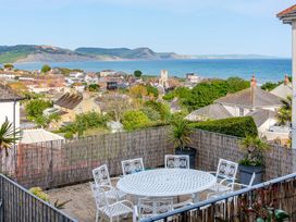 An outdoor space with a table and chairs overlooking the sea and hills at 2 Hadleigh Villas Lyme Regis