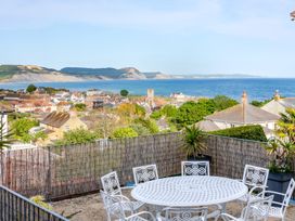 An outdoor dining area with table and chairs overlooking the sea and hills at 2 Hadleigh Villas Lyme Regis