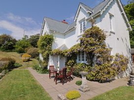 An outdoor patio area with a table and chairs next to a white two-story house with climbing plants and flowers at Lynch Cottage in Rousdon