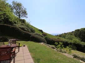 A garden with patio furniture and green hedges overlooking a hillside and distant sea at Lynch Cottage in Rousdon