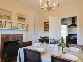 A dining room with a table set for a meal and a view into a kitchen at Lynch Cottage in Rousdon