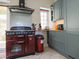 A kitchen with a red stove, matching red bin, grey cabinets, a toaster, microwave, and a window at Lynch Cottage in Rousdon