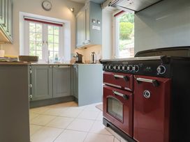 A kitchen with green cabinets a red oven a clock above a window and a door leading outside at Lynch Cottage in Rousdon