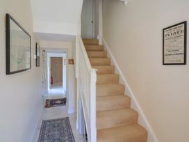 A hallway with stairs carpeted in beige and framed pictures on the walls at Lynch Cottage in Rousdon