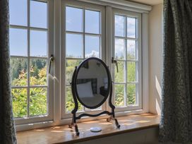 A wooden windowsill with an oval mirror and a view of trees through a window at Lynch Cottage in Rousdon