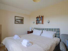 A bedroom with a double bed with white linens and folded towels and a wooden shelf with books above the headboard at Lynch Cottage in Rousdon