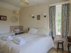 A bedroom with a bed with white linens towels on top a sink with a mirror and floral curtains at Lynch Cottage in Rousdon