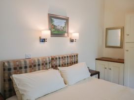 A bedroom with a double bed with checkered headboard two wall lamps a framed picture a mirror and a cabinet at Lynch Cottage in Rousdon