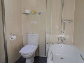 A bathroom with a toilet, bathtub, showerhead, and a glass shelf holding a toilet paper roll and a small box at Lynch Cottage in Rousdon