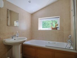 A bathroom with a sink and mirror next to a bathtub under a window with a model ship on the sill at Lynch Cottage in Rousdon