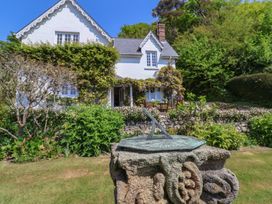 A sundial on a stone pedestal with a white house and garden in the background at Lynch Cottage in Rousdon