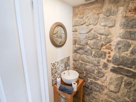 A bathroom with a sink, mirror, wooden table, and stone wall at The Bakehouse in Lyme Regis