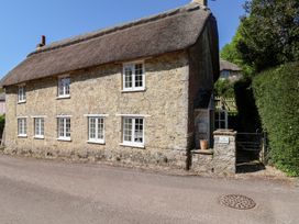 A stone cottage with white framed windows and a thatched roof beside a road at The Gatehouse in Axmouth