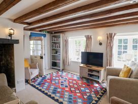 A living room with wooden beams a colorful rug a sofa armchairs a television on a stand and a bookcase at The Gatehouse in Axmouth