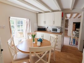 A dining area with a round wooden table and four chairs near cabinets with a microwave and a window at The Gatehouse in Axmouth