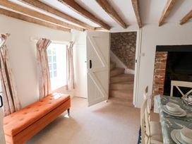 A room with wooden ceiling beams an orange bench near a window stairs a dining table and a brick fireplace at The Gatehouse in Axmouth
