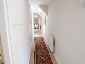 A narrow hallway with a patterned runner rug a radiator on the right wall and a chair and bookshelf visible at the end at The Gatehouse in Axmouth