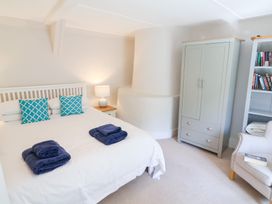 A bedroom with a white bed with blue pillows and folded towels a bedside table with a lamp a grey wardrobe a bookshelf and an armchair at The Gatehouse in Axmouth