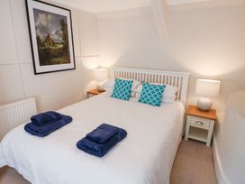 A bedroom with a white bed and blue towels on it two bedside tables with lamps and a framed picture on the wall at The Gatehouse in Axmouth