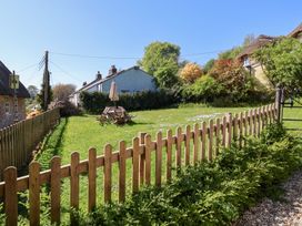 A garden area with wooden fence chairs and table with umbrella near houses with thatched roofs at The Gatehouse in Axmouth