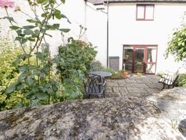 A stone patio with metal table and chairs surrounded by plants and a bench in front of a white house with red framed windows at Mews Cottage in Llanrwst