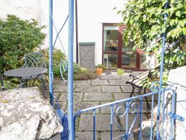 A patio with stone tiles a metal table with two chairs a wooden bench and potted plants at Mews Cottage in Llanrwst