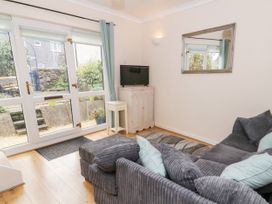 A living room with a gray sofa a small white cabinet with a TV and glass doors leading to a garden at Mews Cottage Llanrwst