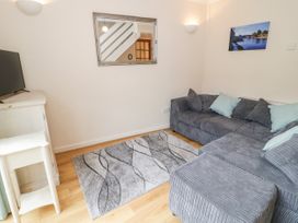 A small living room with a gray sectional sofa with cushions a patterned rug a wall mirror and a television on a white stand at Mews Cottage in Llanrwst