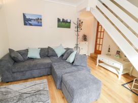 A living room with a gray sectional sofa and ottoman wooden floor and white side tables at Mews Cottage in Llanrwst