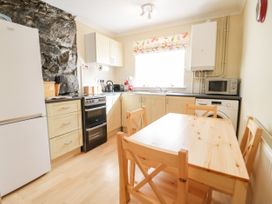 A kitchen with wooden cabinets a stone wall a refrigerator stove wooden table and chairs at Mews Cottage in Llanrwst