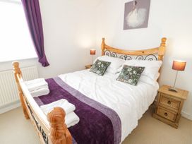 A bedroom with a wooden bed frame white bedding purple throw and curtains two bedside tables with lamps and floral cushions at Mews Cottage in Llanrwst