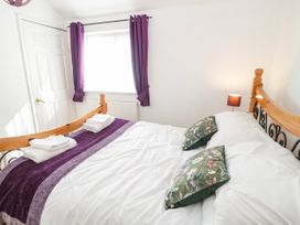 A bedroom with a wooden bed frame white bedding purple curtains and floral pillows at Mews Cottage in Llanrwst