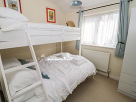 A bedroom with a white bunk bed near a window with blue curtains and a wardrobe in Mews Cottage Llanrwst