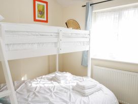 A bedroom with a white bunk bed a window with light blue curtains and folded towels on the bed at Mews Cottage in Llanrwst