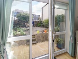 A garden patio with potted plants and outdoor seating viewed through open glass doors at Mews Cottage in Llanrwst