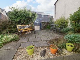 An outdoor patio area with a wooden bench metal table and chairs flower pots and plants at Mews Cottage in Llanrwst