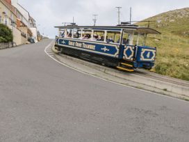 A tram with passengers traveling uphill near houses and grassy hill at Mews Cottage in Llanrwst