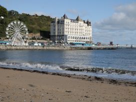 A sandy beach with waves and a waterfront area featuring a ferris wheel and the Grand Hotel building